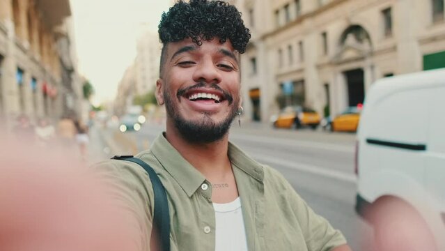Young happy man with beard dressed in an olive color shirt stands next to the road uses smartphone, smiles and makes video call