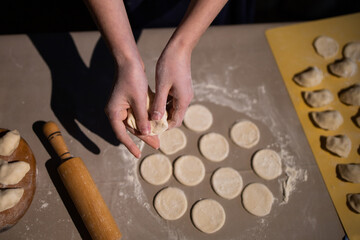Fototapeta na wymiar Sculpt dumplings. Make dumplings in the kitchen. Dough for dumplings. Ukrainian traditional dish. Wooden rolling pin. Hands of a person