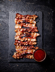 Strips of fried bacon on a stone board with tomato sauce. 