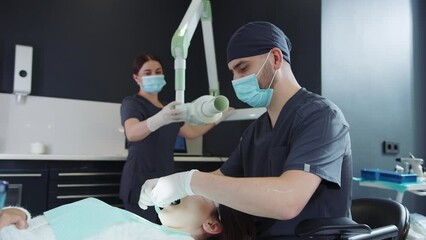 Dentist and assistant preparing for treatment of female patient in protective glasses at modern dental office. Special medical tools and equipment. Indoors. Eye safety