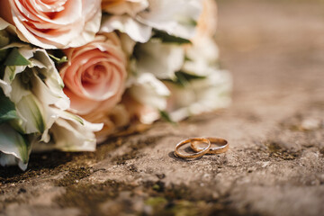 wedding rings and bride's bouquet lie on a stone