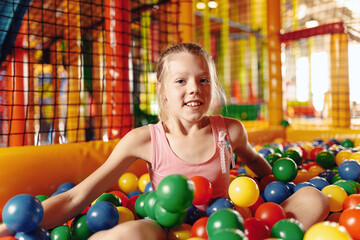Fototapeta na wymiar Happy little girl playing in amusement park balls pool. Kids cheering and playing with plastic colourful balls. Children throwing balls high. Playing with balls: activities for children
