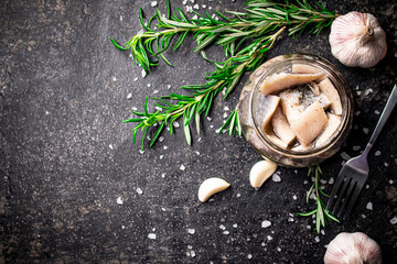 Pieces of salted herring in a glass jar with rosemary and garlic.
