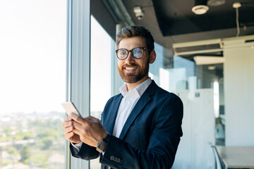 Business and telecommuting concept. Portrait of happy middle aged man using smartphone, texting with client in office