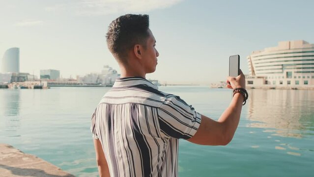 Young man stands on the pier and takes photo on mobile phone