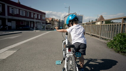 Obraz premium Little boy carrying bicycle outside in city street