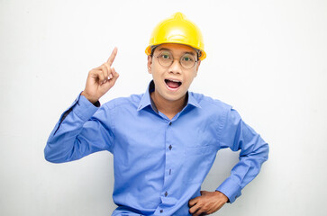 A happy, shocked asian consrtuction worker in blue shirt and yellow safety helmet pointing finger and presenting something ads. 