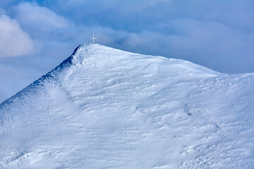 Vom Schnee bedeckte Bergspitze mit einem Kreuz 