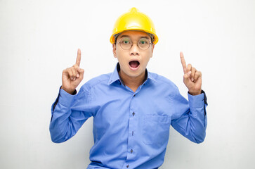 A happy, shocked asian consrtuction worker in blue shirt and yellow safety helmet pointing finger and presenting something ads. 