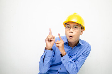 A happy, shocked asian consrtuction worker in blue shirt and yellow safety helmet pointing finger and presenting something ads. 