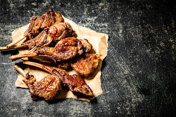 A rack of grilled lamb on paper on the table. 