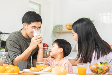 Obraz na płótnie Canvas Happy refreshment family breakfast in morning, asian young parent father, mother and little cute boy, child having meal in kitchen eating together at home. Cheerful, enjoy cooking people.