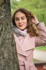 Portrait of a young beautiful long-haired girl in a gray coat in a spring park.