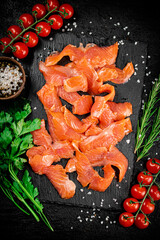 Salted salmon on a stone board with tomatoes and greens. 