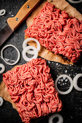 Fresh minced meat on paper on a table with a knife and onion rings.