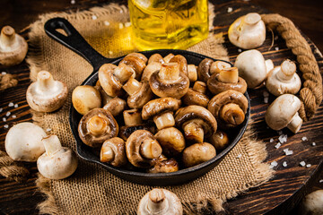 Frying pan with fried mushrooms on a wooden tray. 