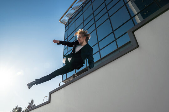 businessman jumping doing parkour with long blonde hair and glasses executive business clothes