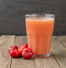 Acerolas or Barbados Cherries juice with fruits over wooden table