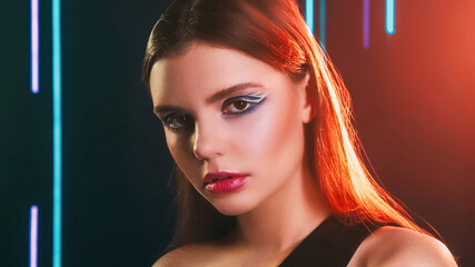 90s beauty. Artistic makeup. 2000s fashion look. Red blue color neon light closeup portrait of teen girl model face with blue eyeshadow pink lips on dark.