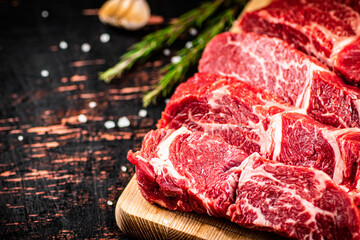 Raw beef on a wooden cutting board with rosemary.