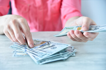 Woman working in ofice and counting usa dollars on table.