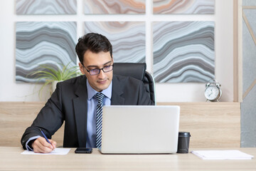 Thoughtful handsome business man working on laptop in the modern office