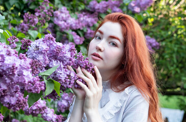 young girl with long red hair in the lilac flowers garden in spring