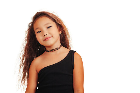 Lovely asian little girl with long curly hair posing at empty background, looking at camera. Studio shot stylish funny small stylish model. Fashion education concept. Copy text space for advertising