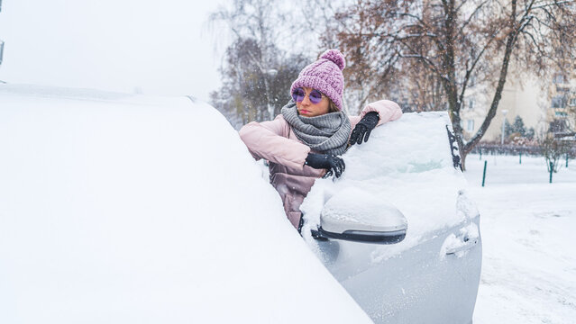 Woman in sunglasses leaning onto open front door of a car under snow . High quality photo