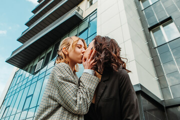 Two pretty women friends posing near glass building. Couple of gay lesbian girls hugging embracing...