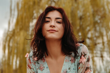 Portrait of charming pretty woman dressed flowery dress posing near willow salix alba tree blossoms blooming in the park in early spring nature. Fashion, girl model with black hair   © Volodymyr