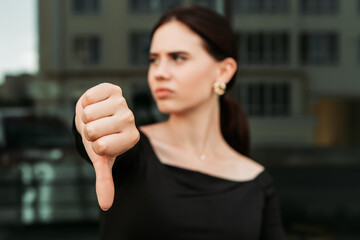 Pretty brunette caucasian woman standing outside street with white teeth beaming healthy lady. Happy millennial girl showing thumb down dislike disapprove sign gesturing making faces

