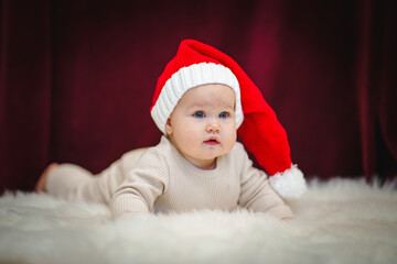 Cute baby in a Santa hat. Christmas mood and new year on a burgundy background. Copy space