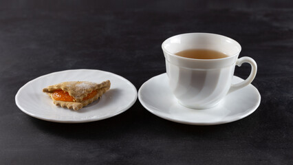 On the table are a cup of tea and cookies. On a dark background. Horizontal frame.