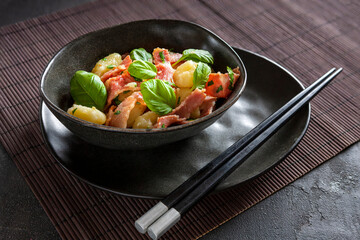 Traditional homemade cooked italian potato gnocchi baked with bacon, parsley served with chopstick on dark gray background.