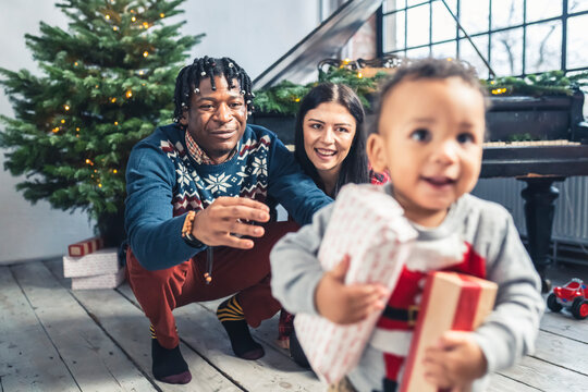 Multiracial young parents and toddler son with presents under a Christmas tree. High quality photo