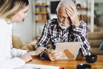 Female home caregiver comforting senior man who is talking about his old photo at home