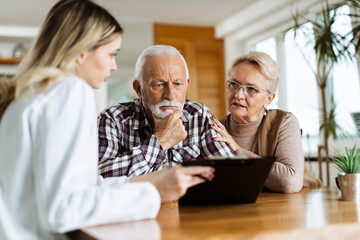 Mature couple looking at their plan of care and medications with female nurse at home