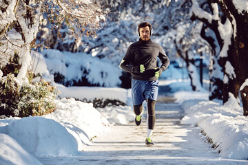 Athlete with headphones running in park during snowy winter day.