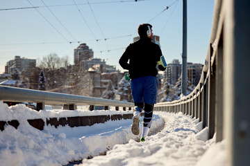 Rear view of athlete running in snow on city streets.