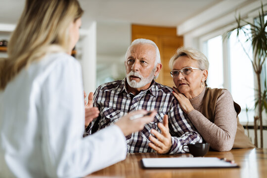 Worried mature couple communicating with female nurse about medical data at home