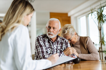 Worried mature couple communicating with female nurse about medical data at home