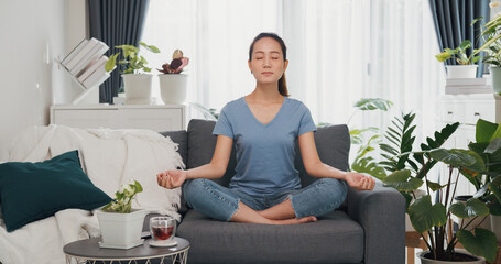 Young Asian woman wear casual site on couch start meditation do yoga feel calm and relax refreshing start new day in living room indoor plants at home. Lifestyle teenager activity concept.