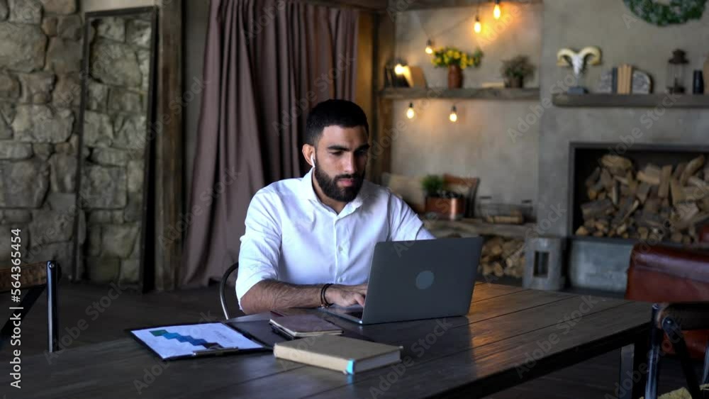 Poster middle eastern male entrepreneur in electronic headphones using laptop computer for online browsing 