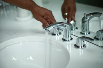 Man turning on a sink faucet with hot water coming out of the tap