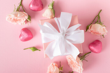 Valentine's Day background. A close-up of a gift, roses and hearts on a light pink background with a space for text.