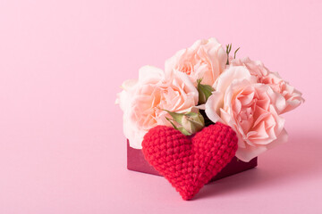 Pink gift box with roses and a knitted red heart on a light pink background with a place for text.