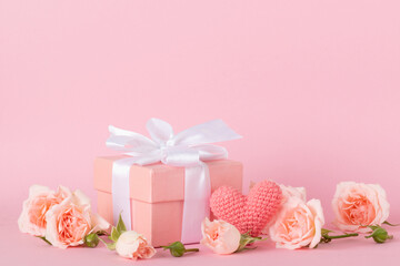 Fototapeta na wymiar Pink gift box with a white bow and a bouquet of roses on a pink background