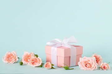 Pink gift box with a white bow and a bouquet of roses on a blue background