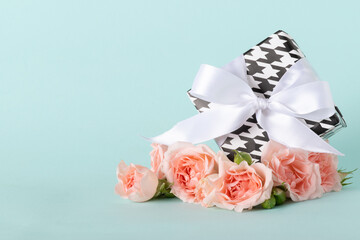 Gift box in black and white with a white bow and a bouquet of roses on a blue background.